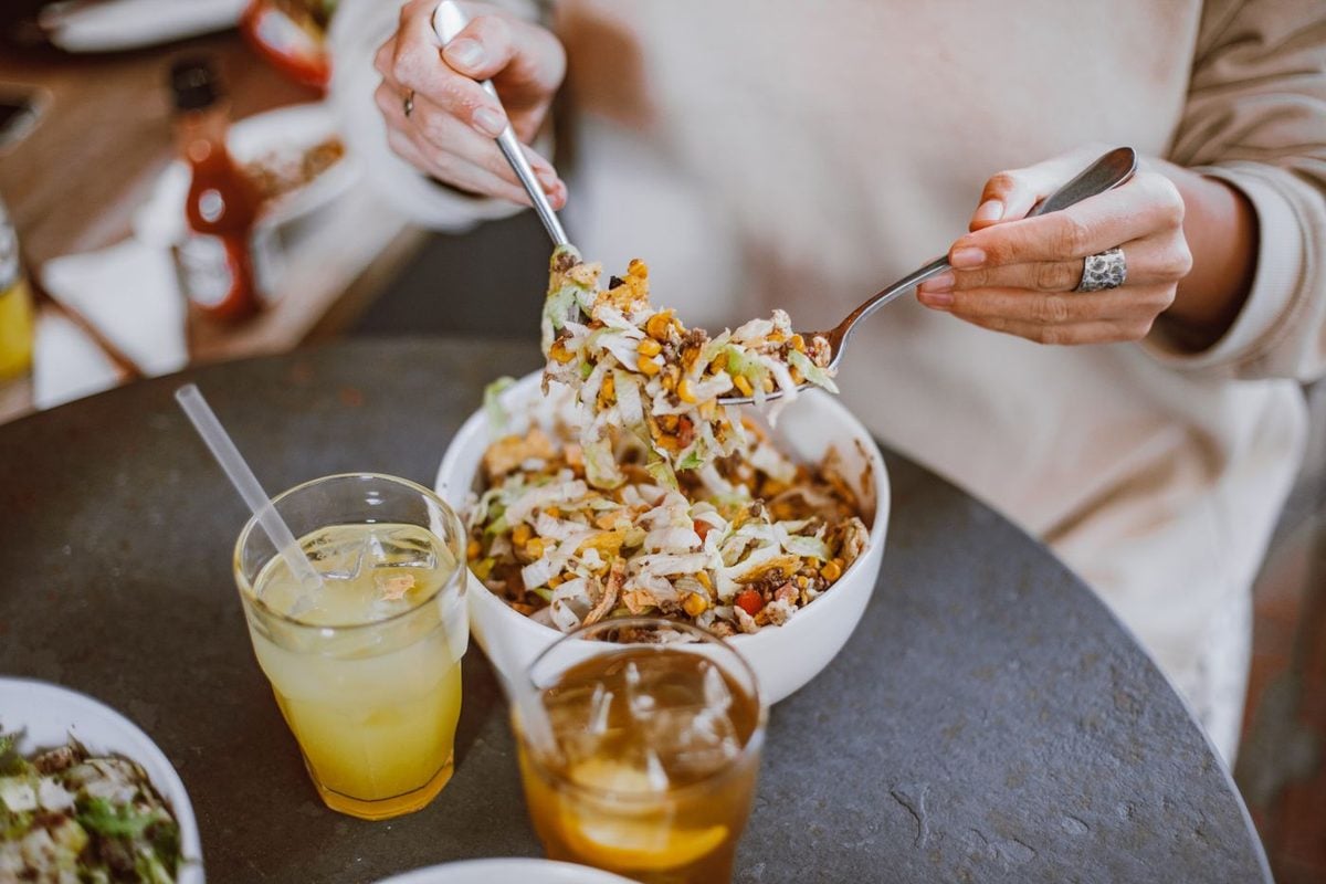 Dos personas comiendo en una mesa con un cuenco de ensalada y vasos de bebida