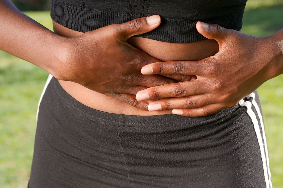 Hinchazón después de comer: qué la provoca de verdad y cuándo no es cosa de la dieta Mujer con ropa deportiva sujetándose el abdomen con las dos manos al aire libre