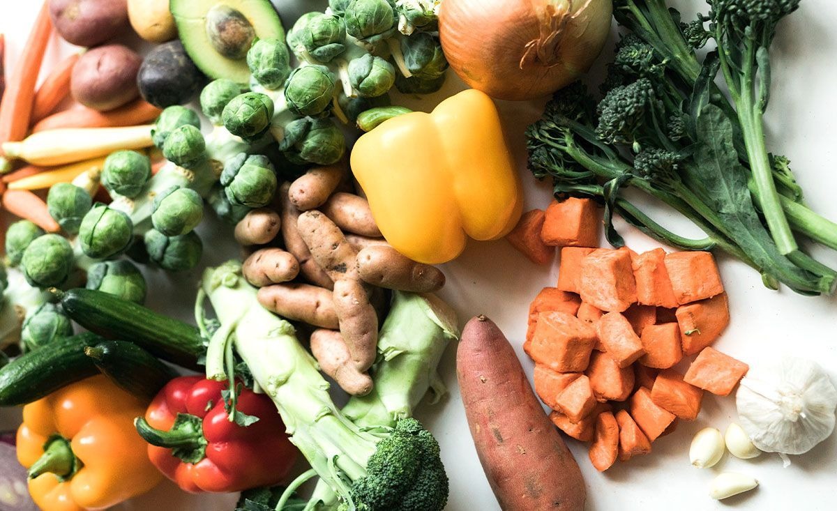 Coles de Bruselas, brócoli, pimientos, boniato, patata, cebolla, ajo, calabacín, aguacate y zanahoria sobre una mesa de madera